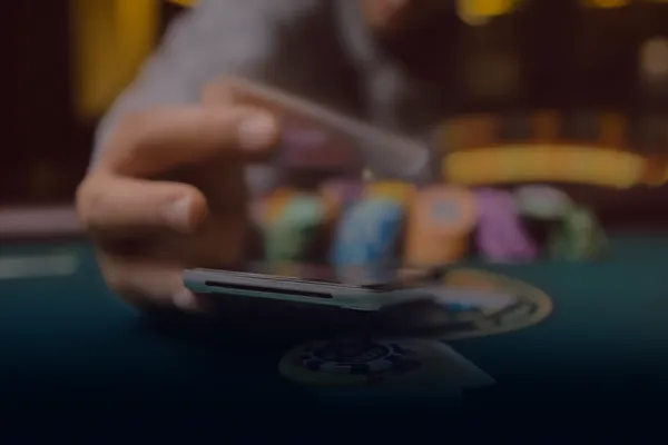 Casino temalı bir arka planda cihaz kullanan bir kişi, NEMESIS BET’e kolay geri dönüş sürecini gösterir.